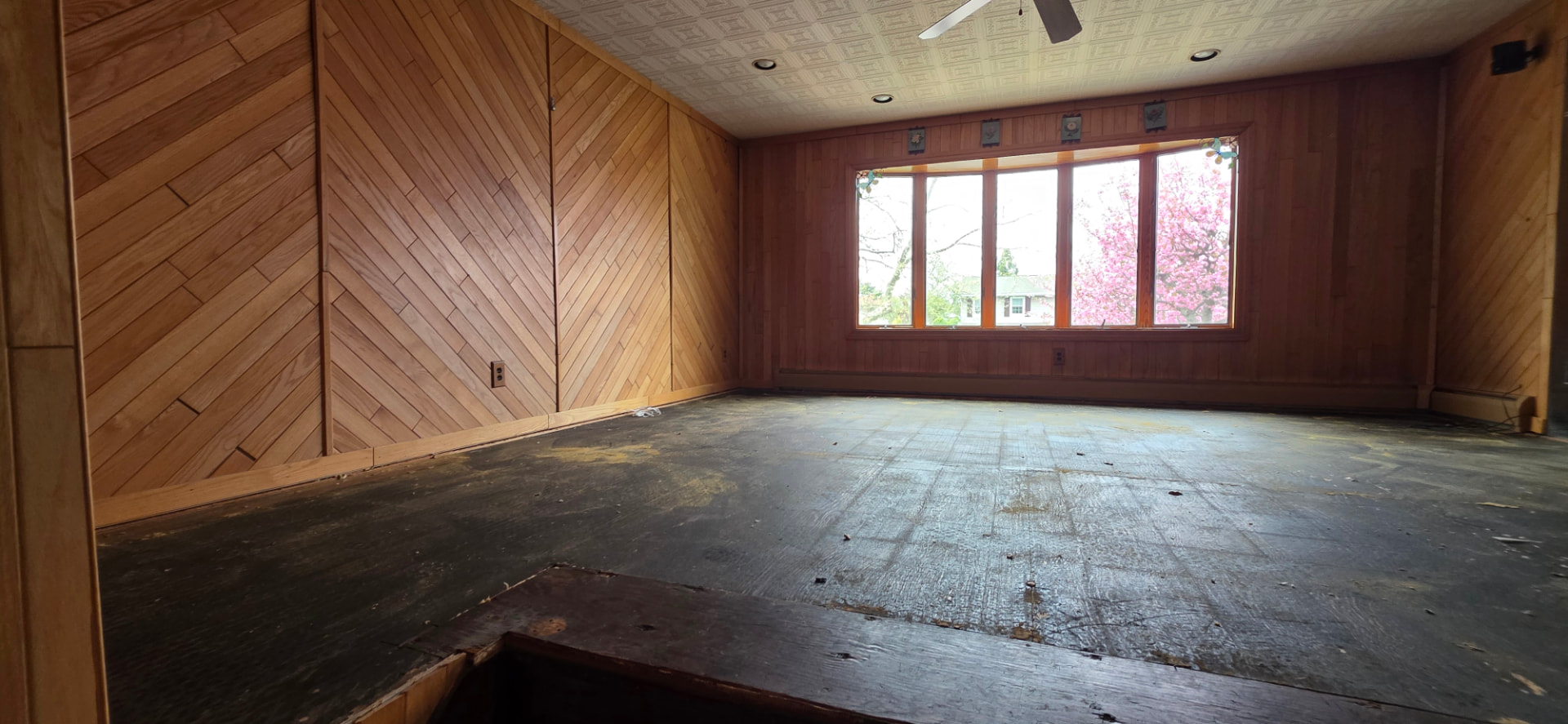 Living room before the work began, with bare subfloor and dated wood paneling