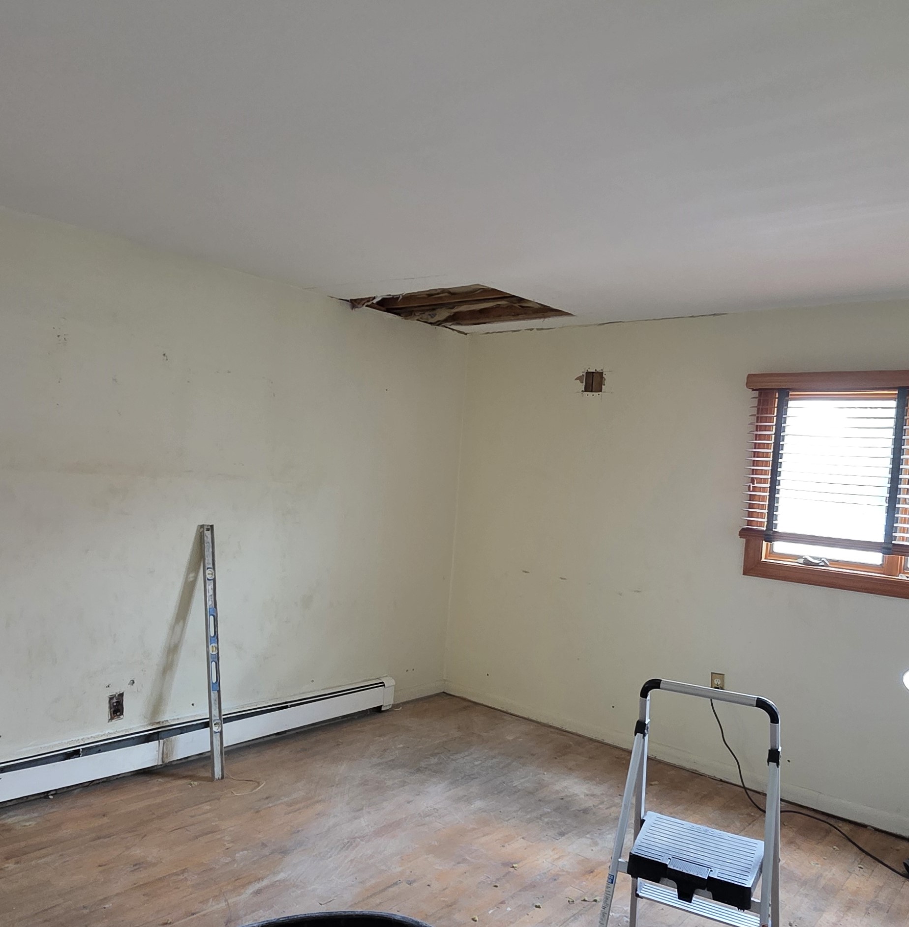 Primary bedroom before the work began, with an open ceiling hole from a leak and worn flooring